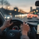 Handen van een jonge bestuurder op het stuur bij schemering, smartphone in houder, met de wijzigingen voor automobilisten in 2026