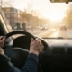Jonge bestuurder met handen aan het stuur rijdt tegen laagstaande zon in tijdens de ochtendspits