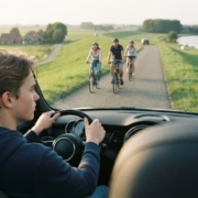 Jonge bestuurder rijdt langzaam op een smalle dijkweg en passeert fietsers