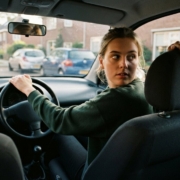 Jonge bestuurder kijkt over haar schouder tijdens fileparkeren in een lesauto