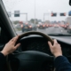 Handen van een jonge bestuurder aan het stuur tijdens het rijden in de spits, met file en remlichten op de snelweg