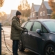 Jonge bestuurder koppelt laadkabel los van elektrische auto in de kou op een herfstochtend